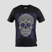A black T-shirt features an intricate skull design with floral and geometric patterns in white and blue. The skull is stylized with ornate details highlighting the eyes, nose, and mouth, creating a visually striking effect against the dark fabric.
