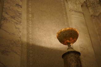 Close-up of an ornate antique vase displayed on a marble pedestal in warm lighting.