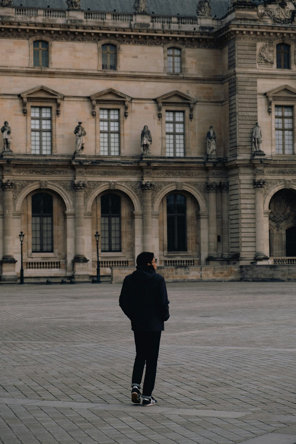 person wearing black jacket standing near Louvre Museum in Paris France during daytime