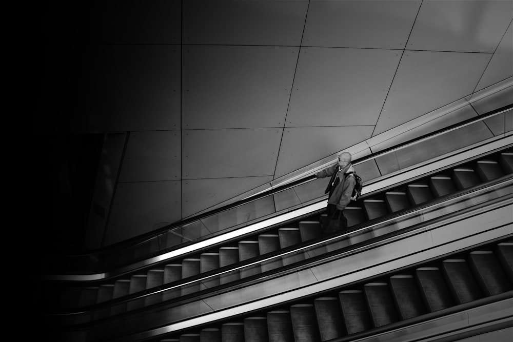 greyscale photography of person standing on escalator