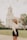 woman wearing white long-sleeved crop top standing near road viewing white church during daytime