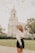 woman wearing white long-sleeved crop top standing near road viewing white church during daytime