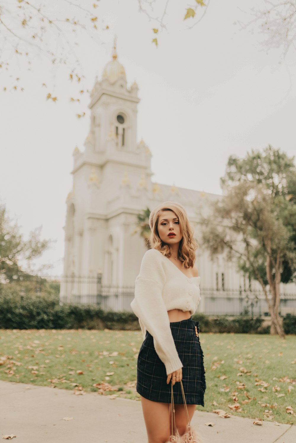 woman wearing white long-sleeved crop top standing near road viewing white church during daytime