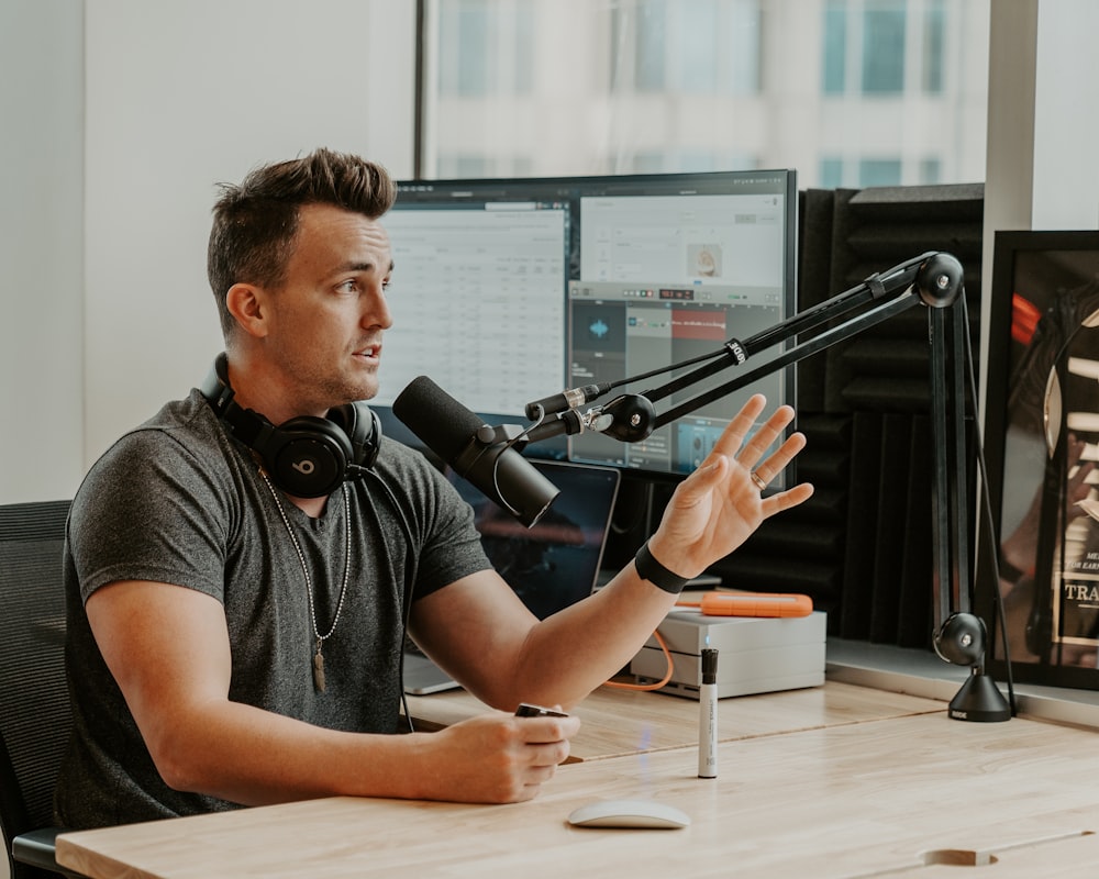 man wearing grey shirt sitting by the table using microphone