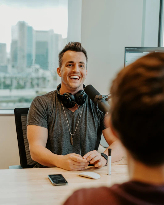 man wearing gray V-neck t-shirt with black headphones on neck sitting and laughing