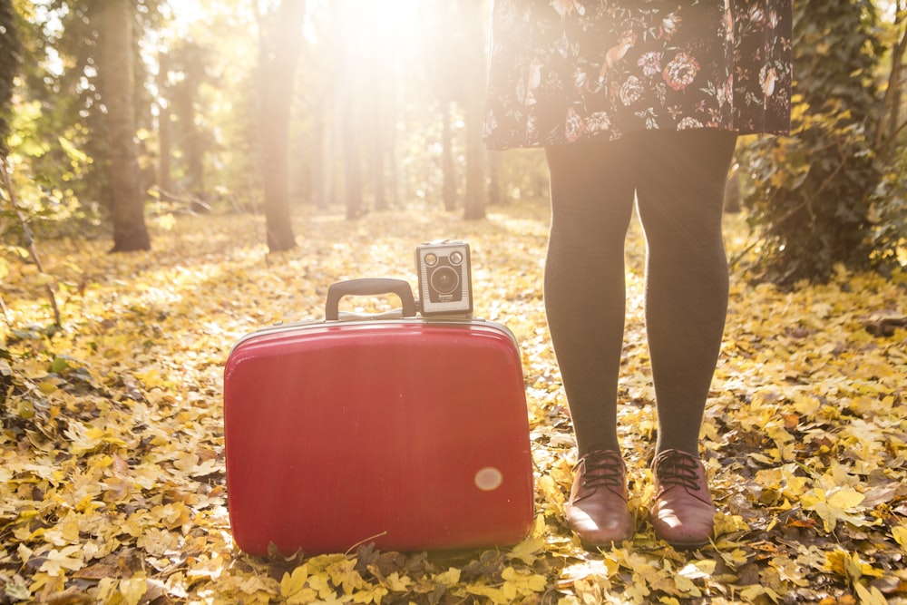 femme debout à côté d’une valise rouge et d’un appareil photo