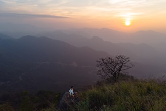 A traveler sitting on a cliff edge, gazing out over rolling hills bathed in soft morning light.