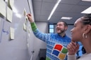 man wearing blue Windows sweater holding sticky note on white board