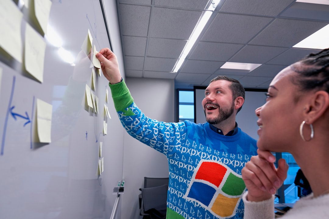 man wearing blue Windows sweater holding sticky note on white board