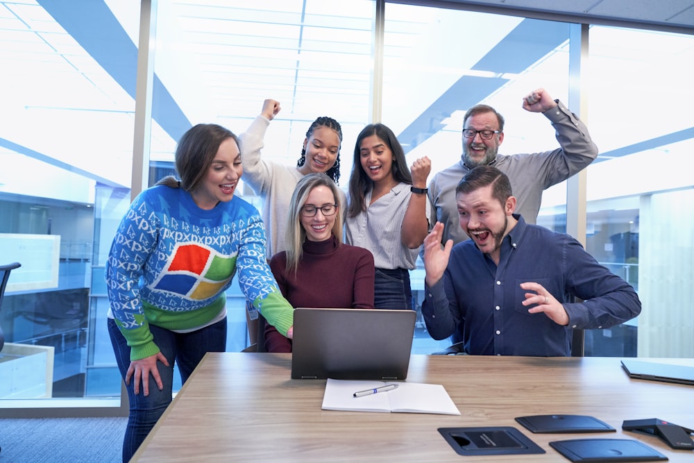 Männer und Frauen, die am Tisch sitzen und stehen und glücklich aussehen, während sie auf den Laptop starren