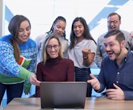 men and women sitting and standing while staring at laptop