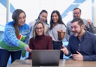 men and women sitting and standing while staring at laptop