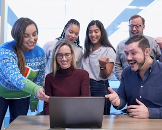 men and women sitting and standing while staring at laptop