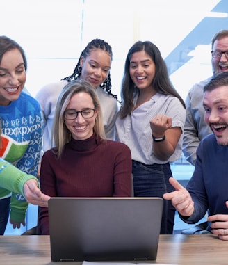 men and women sitting and standing while staring at laptop