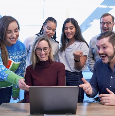 men and women sitting and standing while staring at laptop