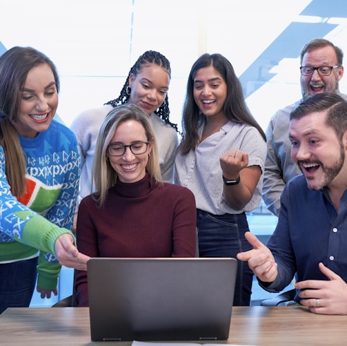 men and women sitting and standing while staring at laptop