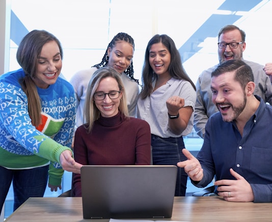 men and women sitting and standing while staring at laptop