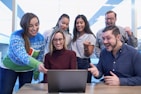men and women sitting and standing while staring at laptop