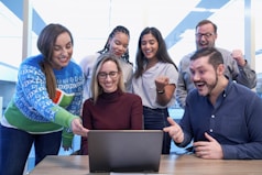 men and women sitting and standing while staring at laptop