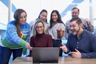 men and women sitting and standing while staring at laptop