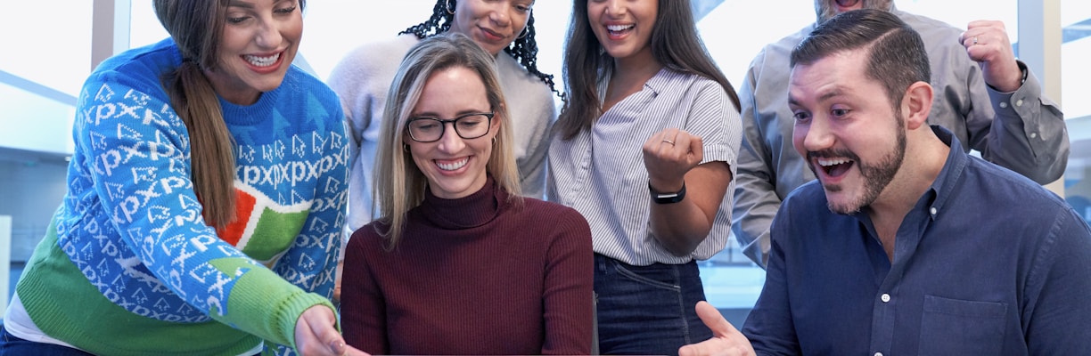 men and women sitting and standing while staring at laptop