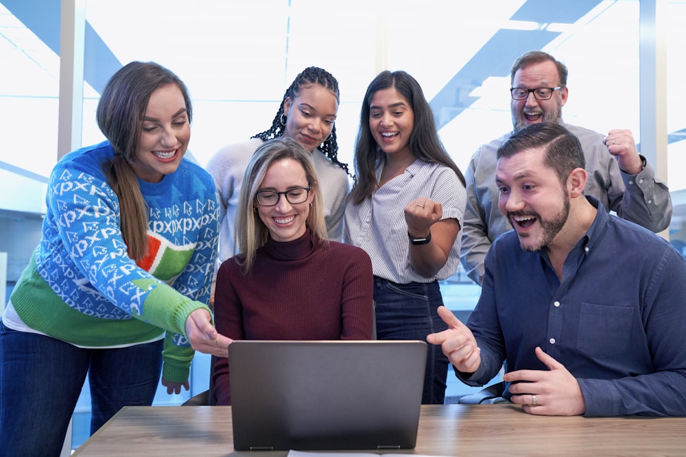 homens e mulheres sentados e em pé enquanto olham para o laptop