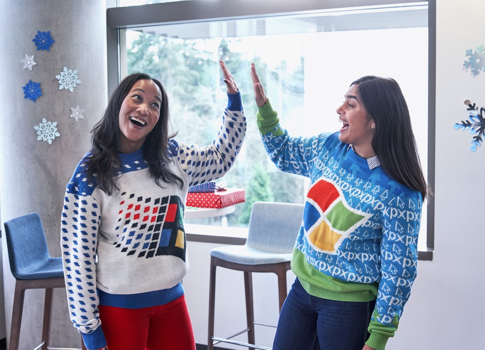 two women in white and blue sweaters doing high five