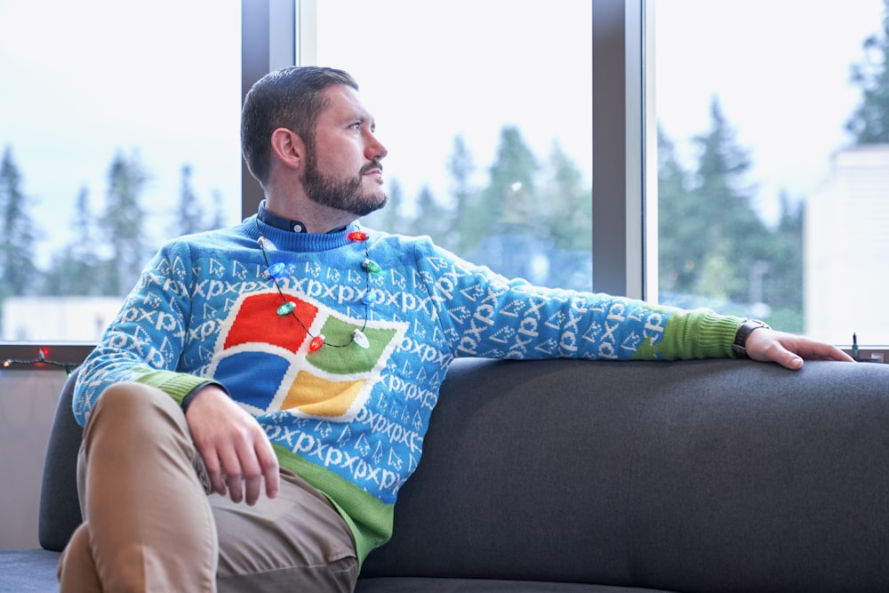 man in blue sweater sitting on sofa beside window