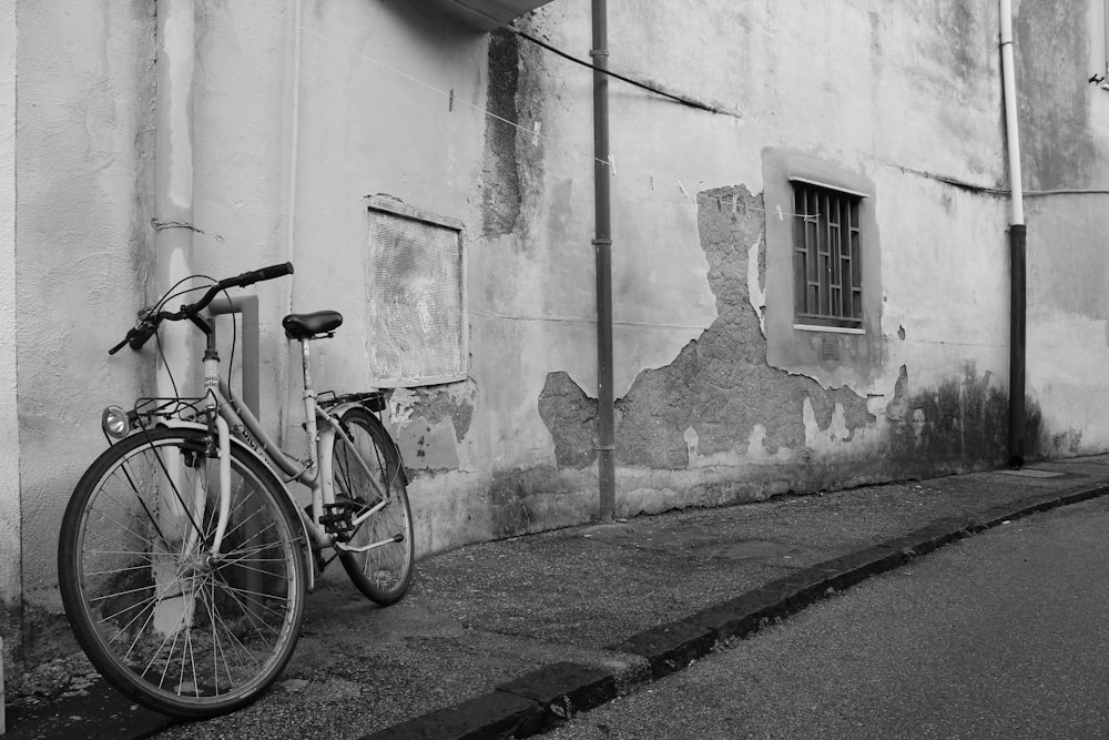 grayscale photography of bicycle parked beside wall