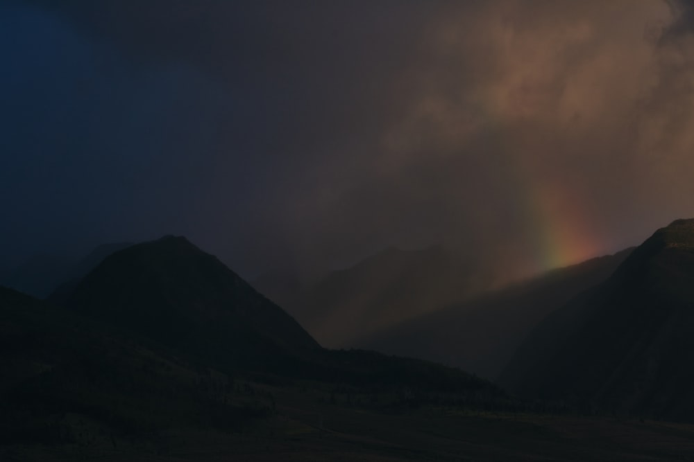 a rainbow shines in the sky above a mountain range