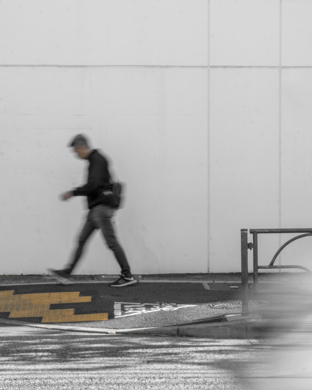 a man walking down a street next to a white wall