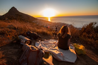 woman sitting on blanket near sea and mountain during dawn