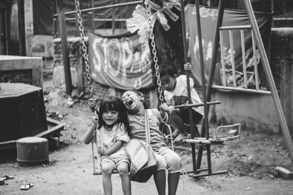 grayscale photography of two child riding on swing