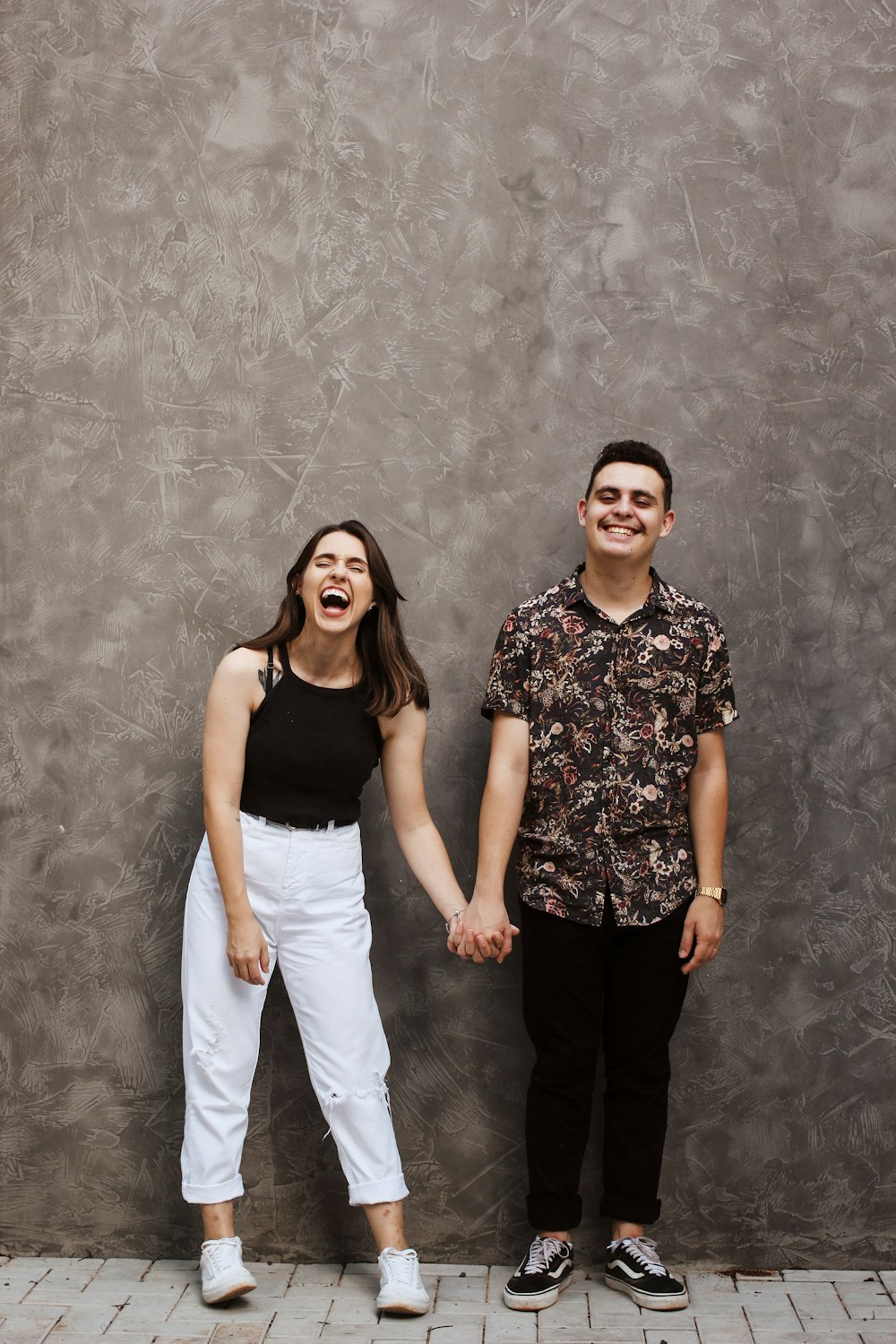 woman and man holding hands near grey wall