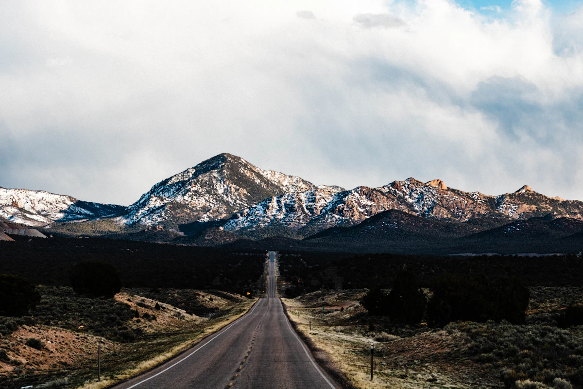A straight two-lane road through sagebrush toward snow-dusted peaks near Cedar City