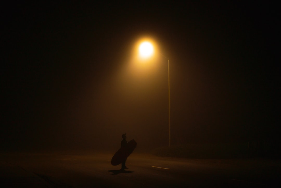 person with surfboard near lamppost turned on during night