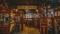 An ornate and intricately designed interior of a traditional pub or bar, featuring rich wooden paneling with carvings, vintage-style lamps, and detailed floor tiles. The space is divided by wooden partitions and cozy seating areas, giving it an intimate atmosphere.