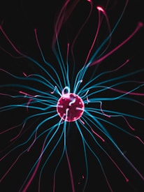 A glowing plasma ball emitting vibrant pink and blue tendrils of light against a dark background. The central sphere is surrounded by dynamic, colorful arcs of electricity that create a captivating visual effect.