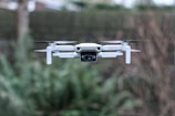 white camera drone flying over green leafed plant