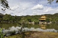 Golden sunlight reflecting off the shimmering Kinkaku-ji temple pond surrounded by lush greenery.