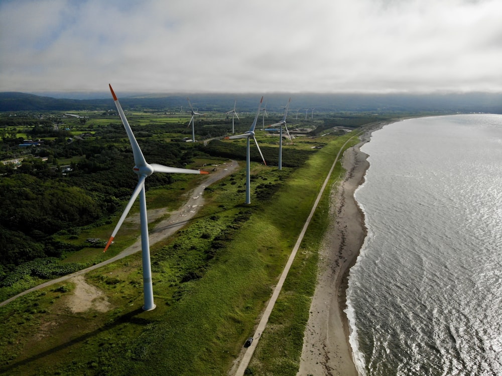 Fotografía aérea de molinos de viento blancos cerca de un cuerpo de agua bajo un cielo blanco y azul