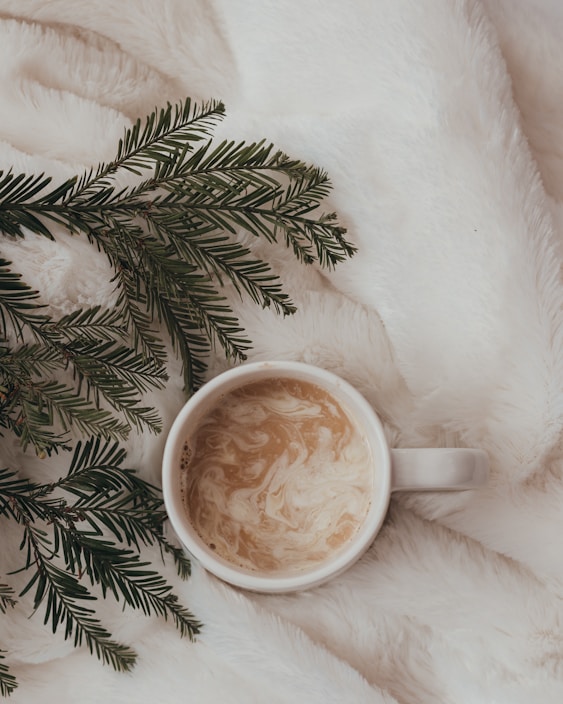 A pair of cotton slippers beside a steaming cup of tea on a cozy knitted blanket.