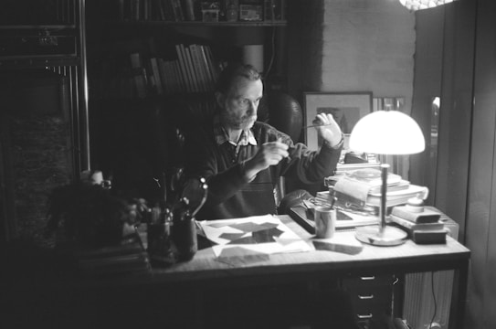 A focused scholar reading a manuscript with a pen in hand, surrounded by books.