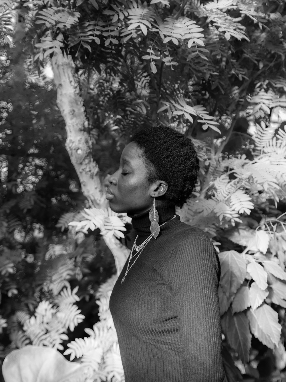 grayscale photography of woman standing while facing her right side near plants