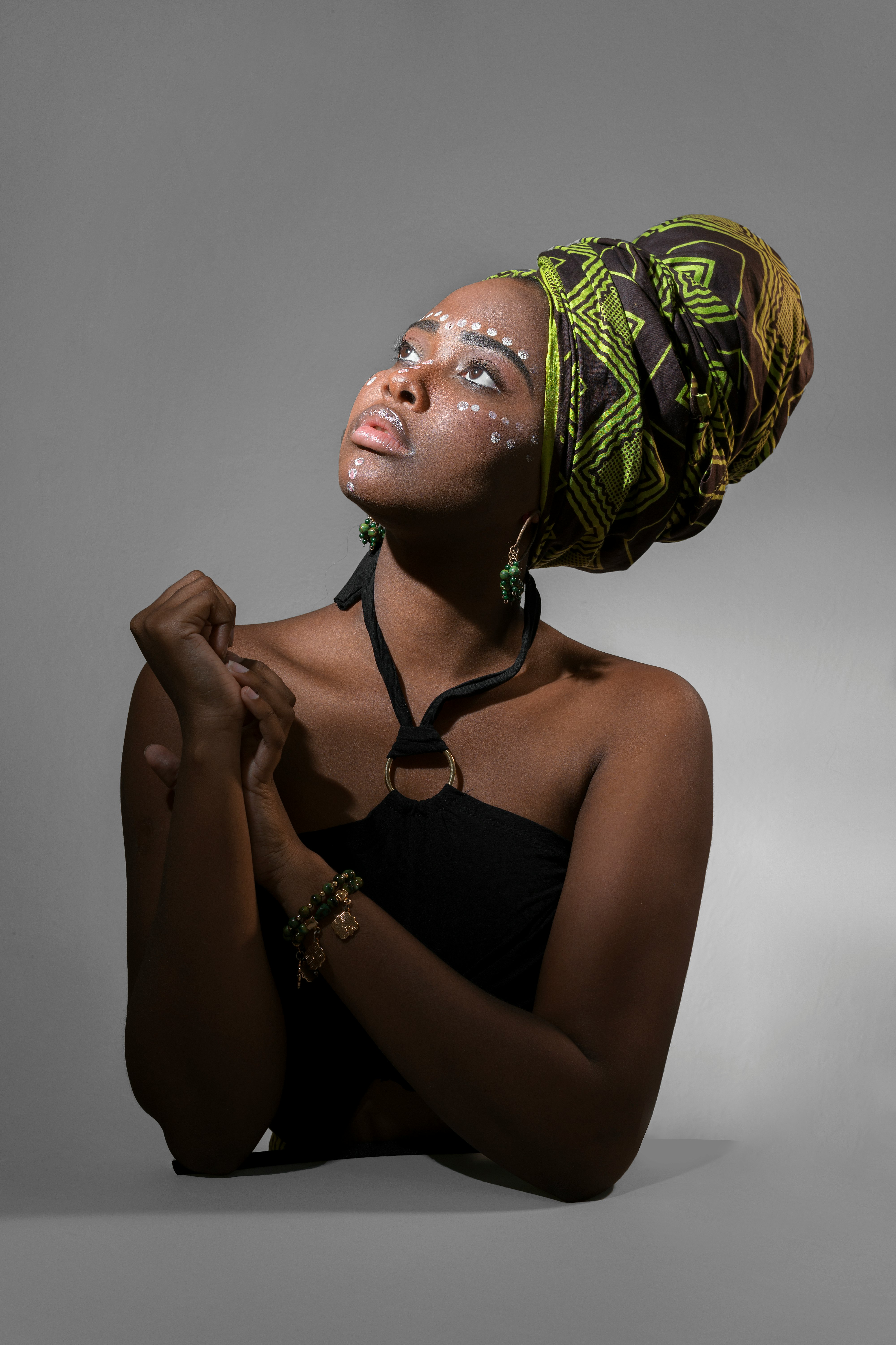 woman wearing black halterneck top and green and gray turban hat looking up