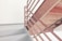 A metal staircase with brown railings and light gray steps is positioned against a plain white wall. The staircase appears to be part of an indoor structure, reflecting minimalistic design elements.