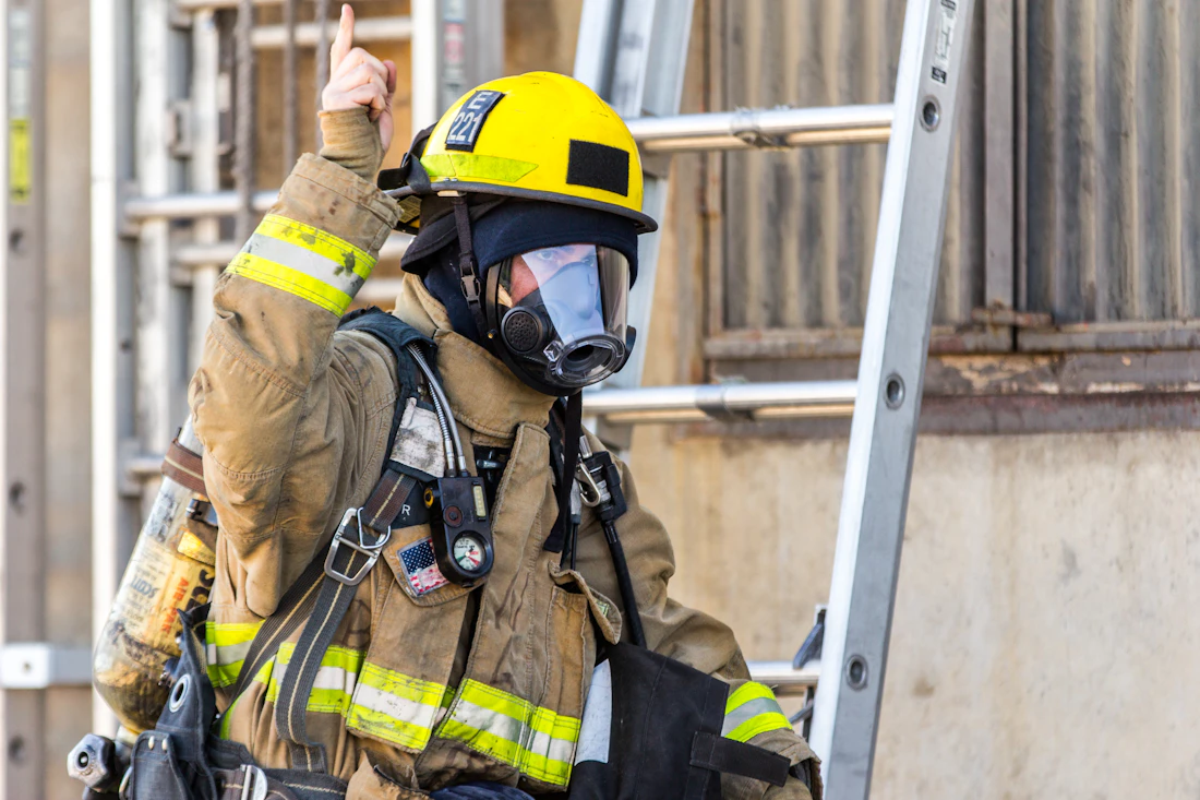 Bombero con casco amarillo y equipo de respiración frente a una escalera, listo para actuar
