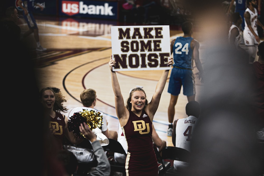 smiling woman standing while holding banner with make some noise print