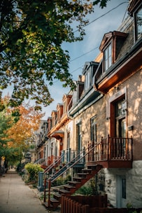 A row of cozy townhomes with front stoops and shared pathways, surrounded by mature trees.