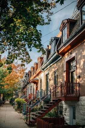 A row of cozy townhomes with front stoops and shared pathways, surrounded by mature trees.